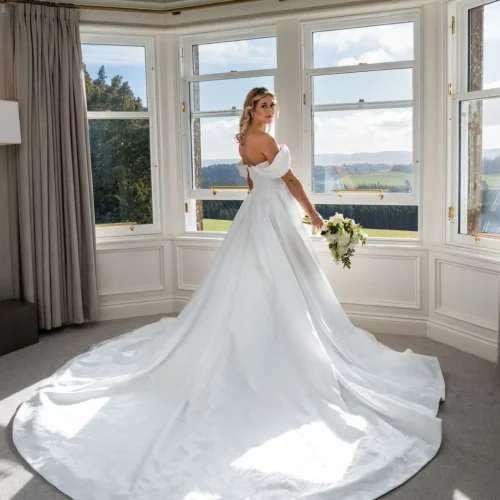 Bride standing in the feature bay window of Kinclune House Bridal Suite with panoramic views across the Vale of Strathmore. Dress by The Hitching Post Bridal. Photography by ZibiZPhoto.