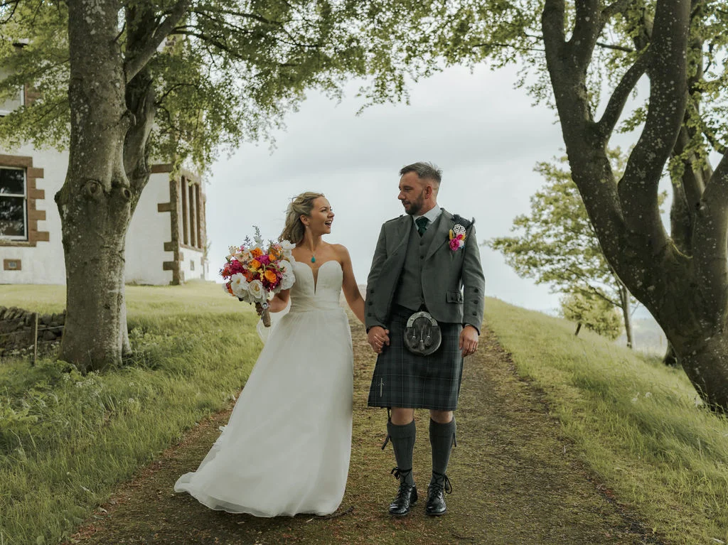 Couple walking hand in hand along a tree‑lined path at Kinclune House & Estate on their wedding day.