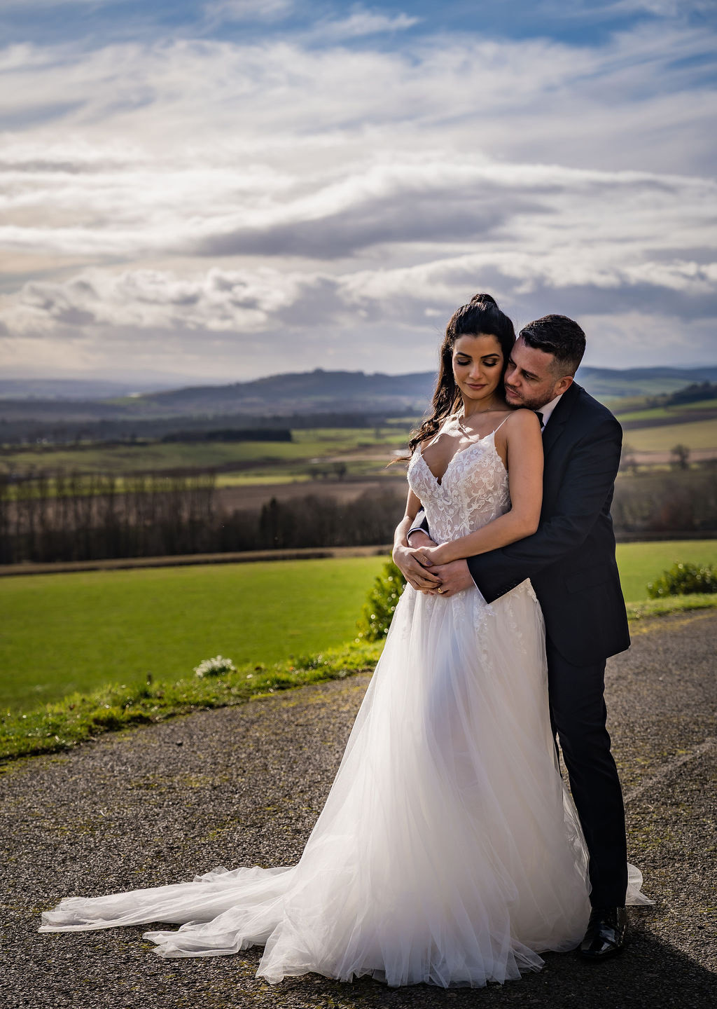 Bride and groom embrace on Kinclune Estate, with sweeping views across the Vale of Strathmore. Dress by The Hitching Post Bridal. Photography by ZibiZPhoto.